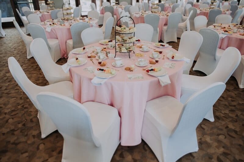 party room with round tables pink linen white chair covers with white plates and fruit skewer at succulent party